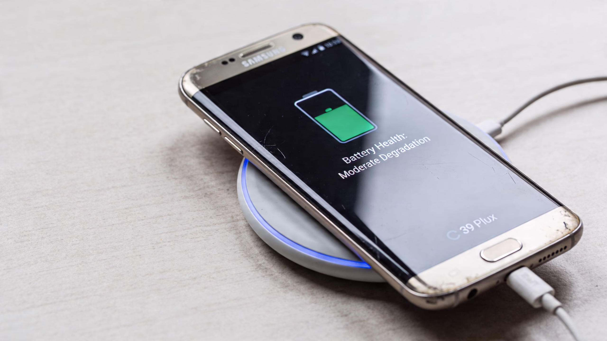 A Samsung smartphone placed on a wireless charging pad, displaying a battery health notification on the screen.